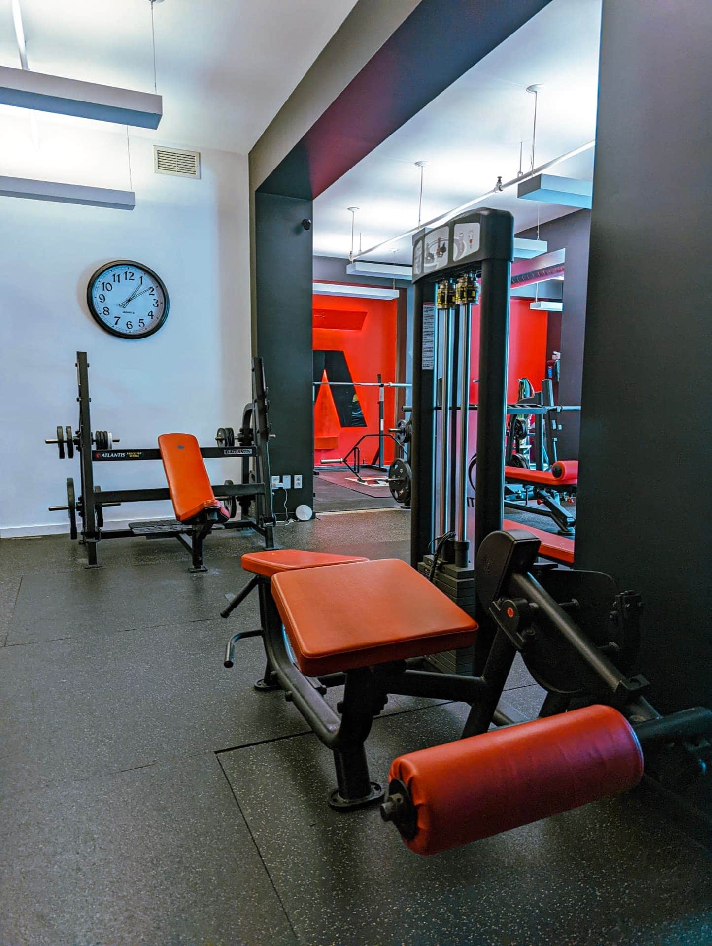 Two training zones at Arzadon Fitness showing white studio area and red-accent main floor with wall clock