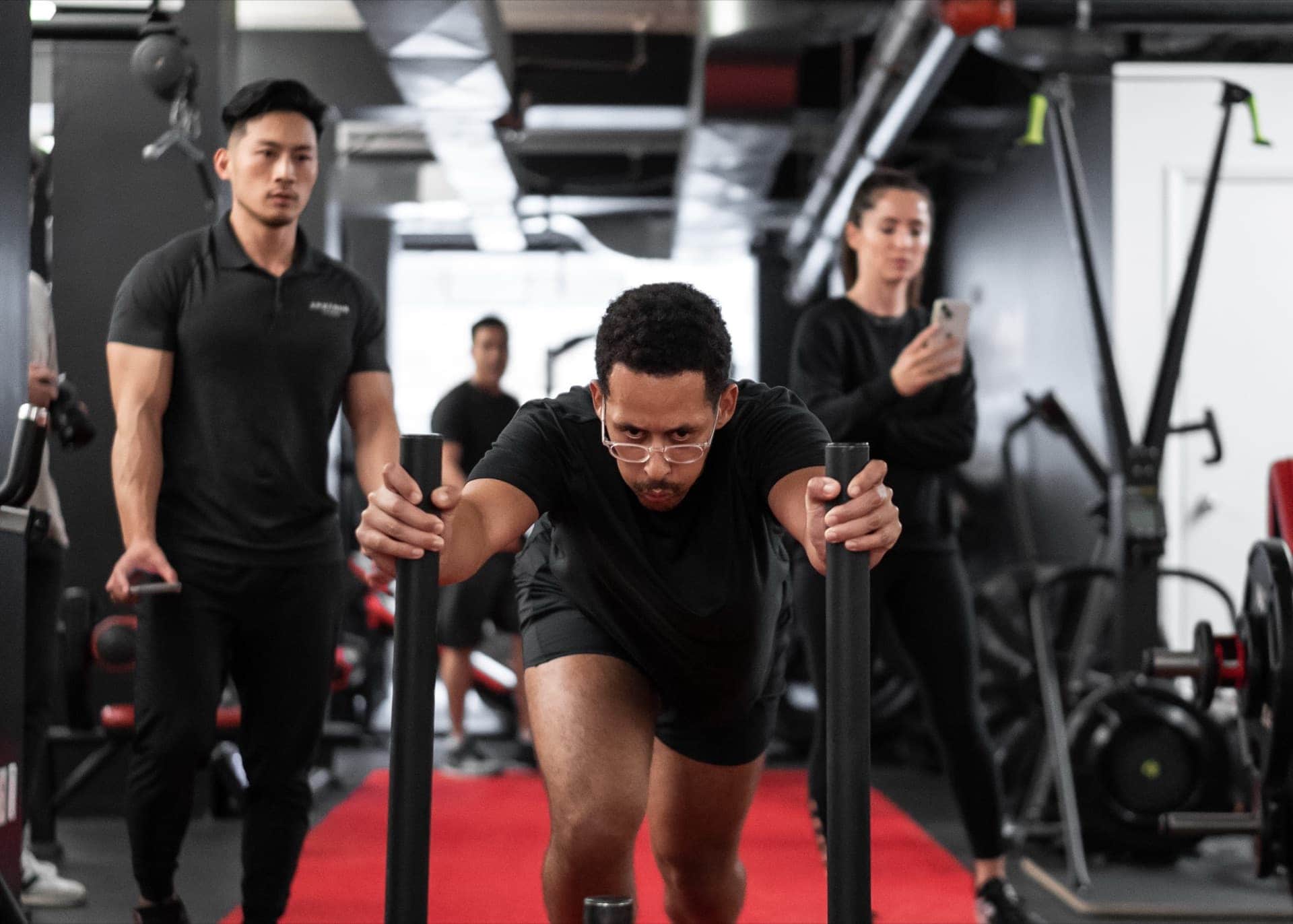 Male athlete sled pushing while coaches observe and film at Arzadon Fitness Toronto