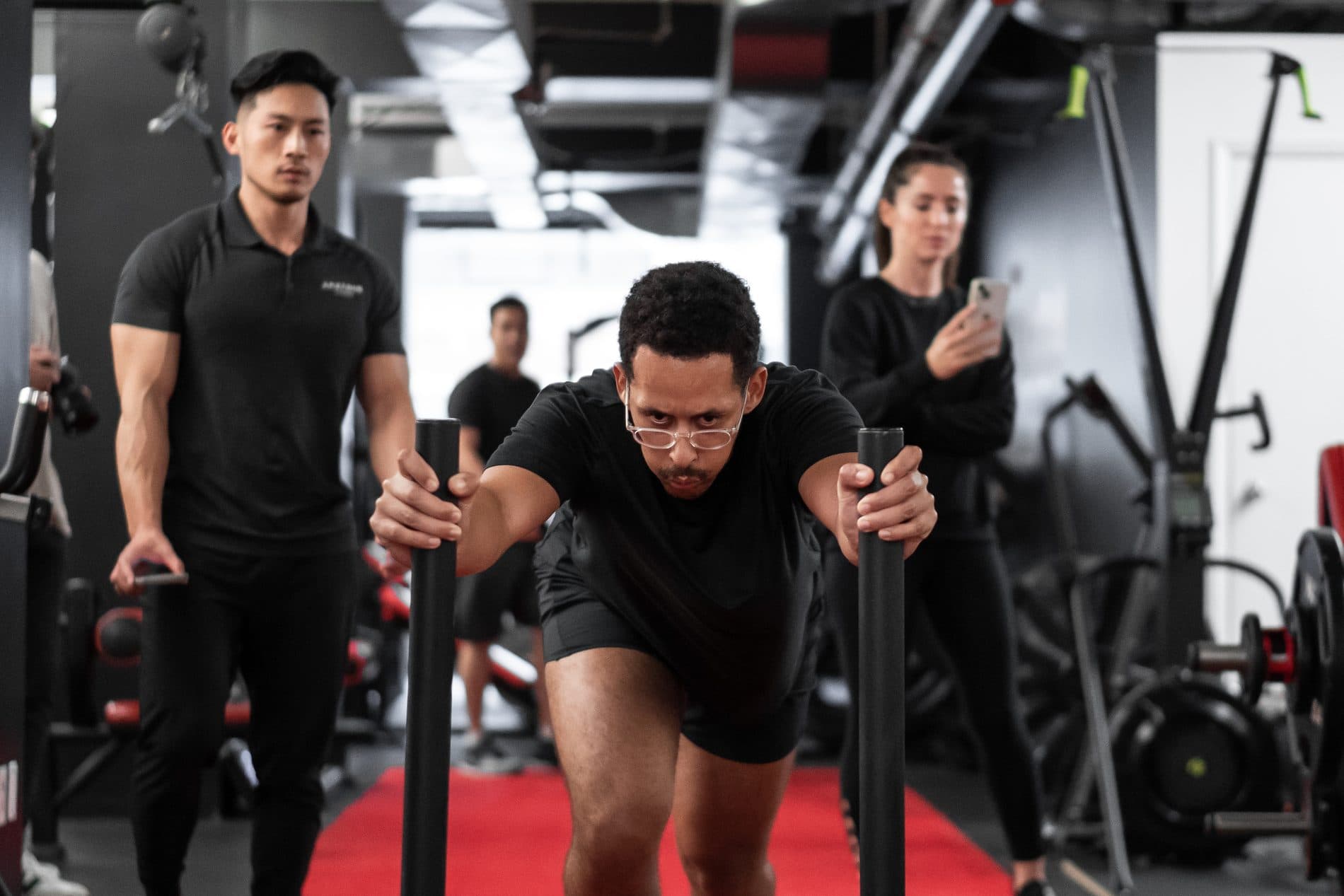 Personal trainer coaching a male client through a sled push conditioning drill on the red turf — personal trainer in King West Toronto at Arzadon Fitness
