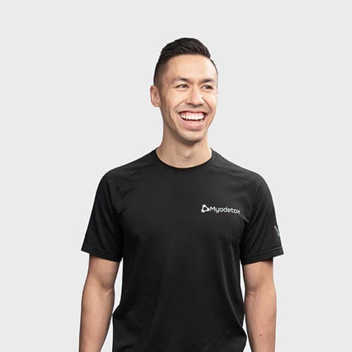Ethan Lee RMT smiling in full-torso professional headshot wearing Myodetox shirt
