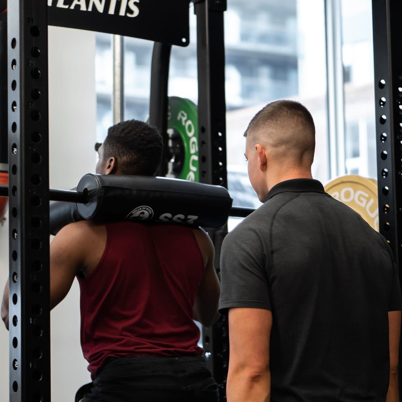 Personal trainer coaching a male client through a safety-bar squat in the power rack at Arzadon Fitness Toronto