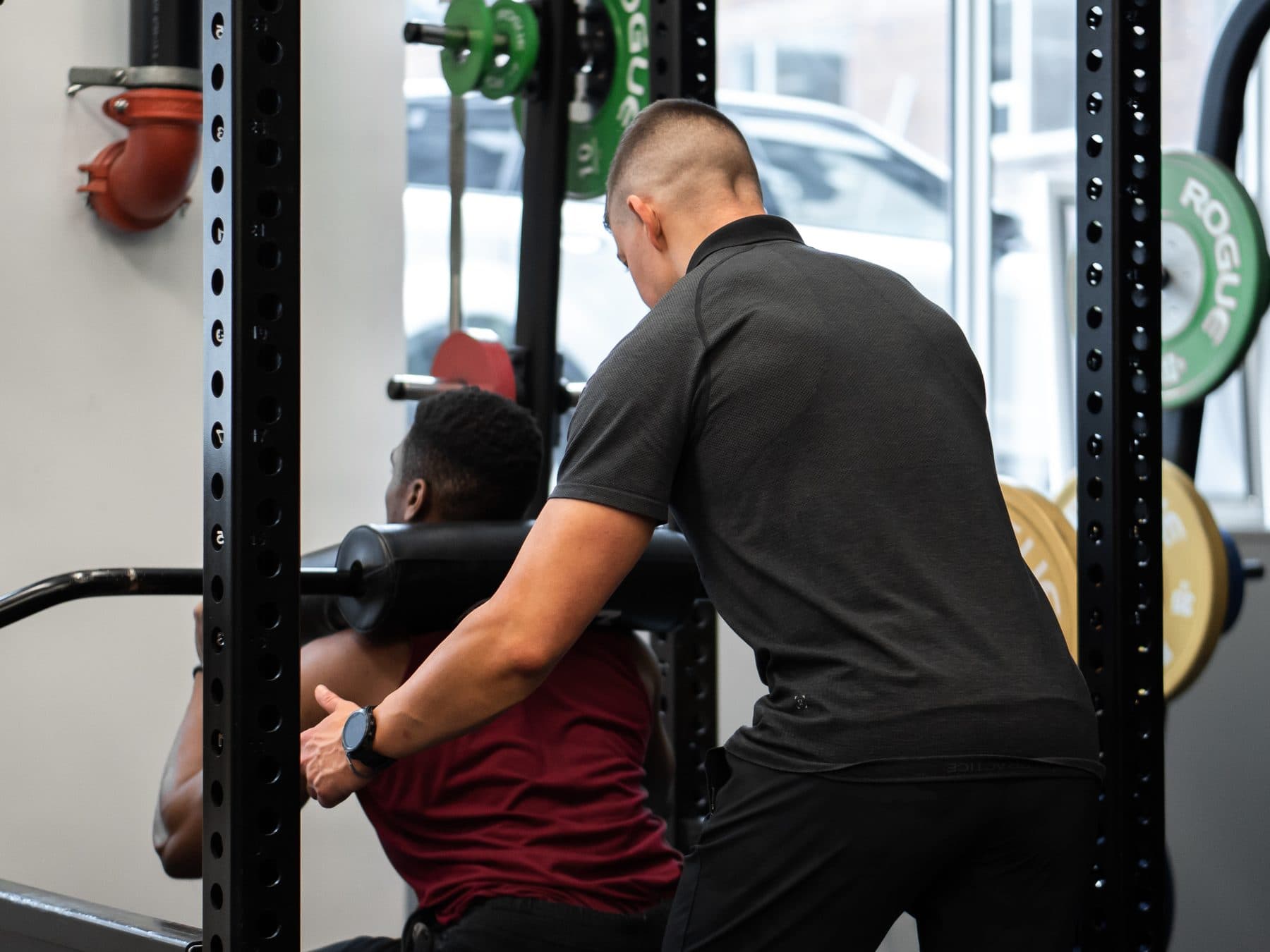 Personal trainer spotting a male client through a barbell squat in the power rack at Arzadon Fitness hybrid coaching gym in King West Toronto
