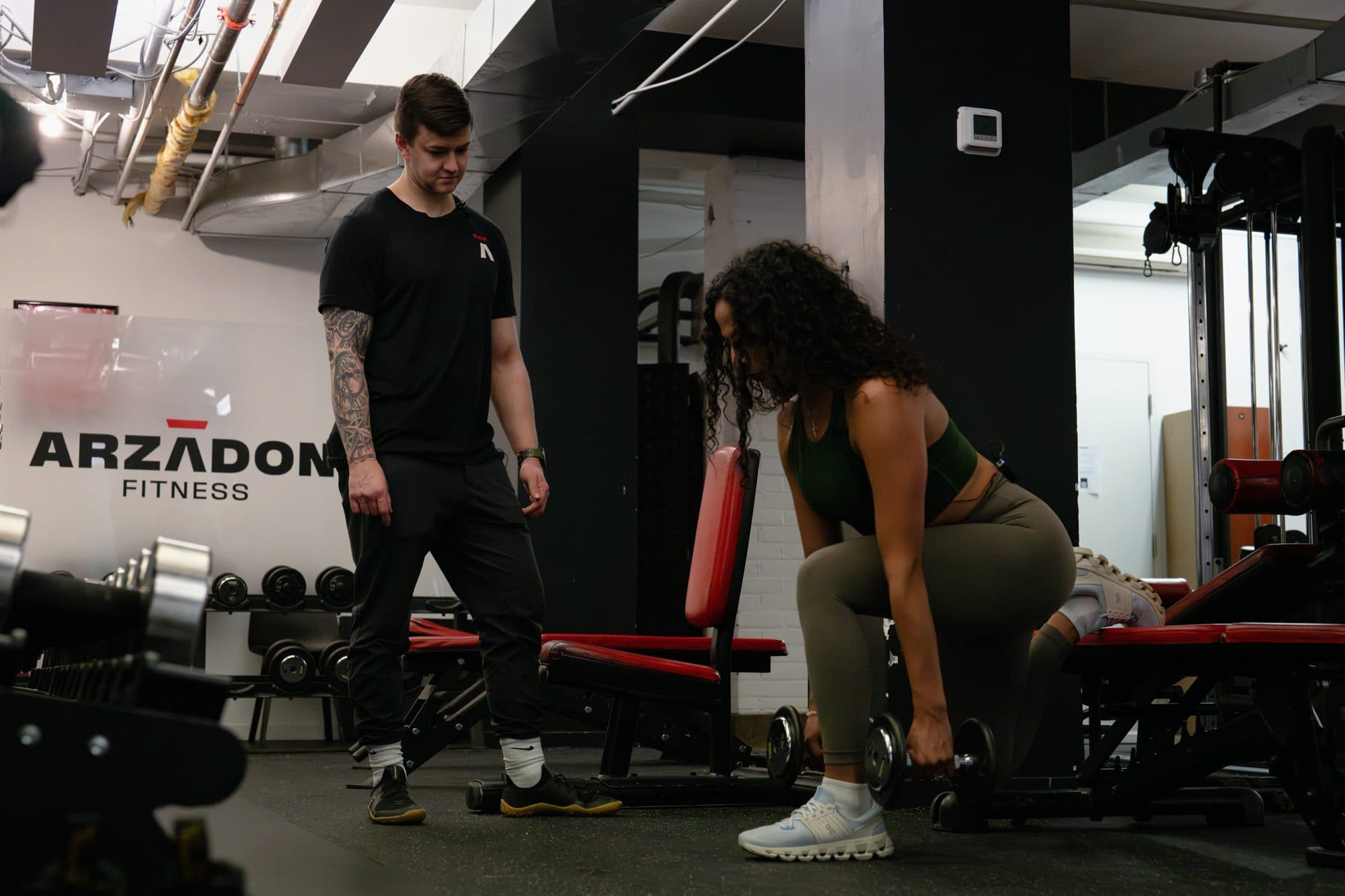 Arzadon Fitness coach supervising a client's dumbbell row form during a personal training assessment in Toronto