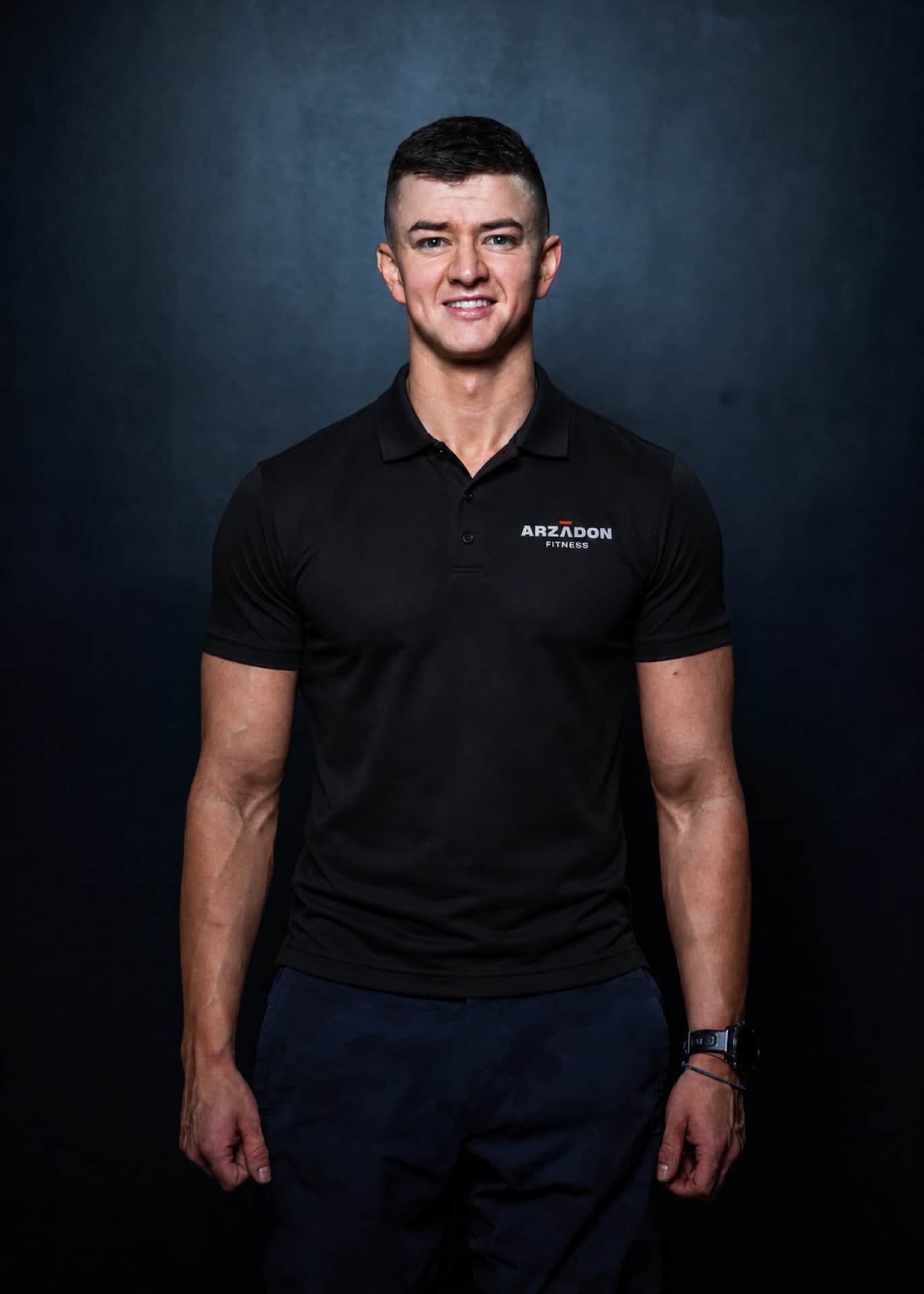 Stuart Charlesworth, Senior Transformation Expert, in Arzadon Fitness polo with slight angle stance against dark studio background